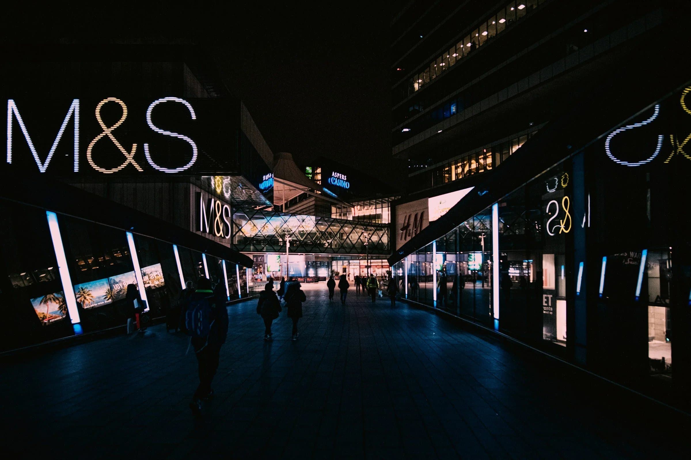 Illuminated shopfronts along a shopping-centre walkway at night