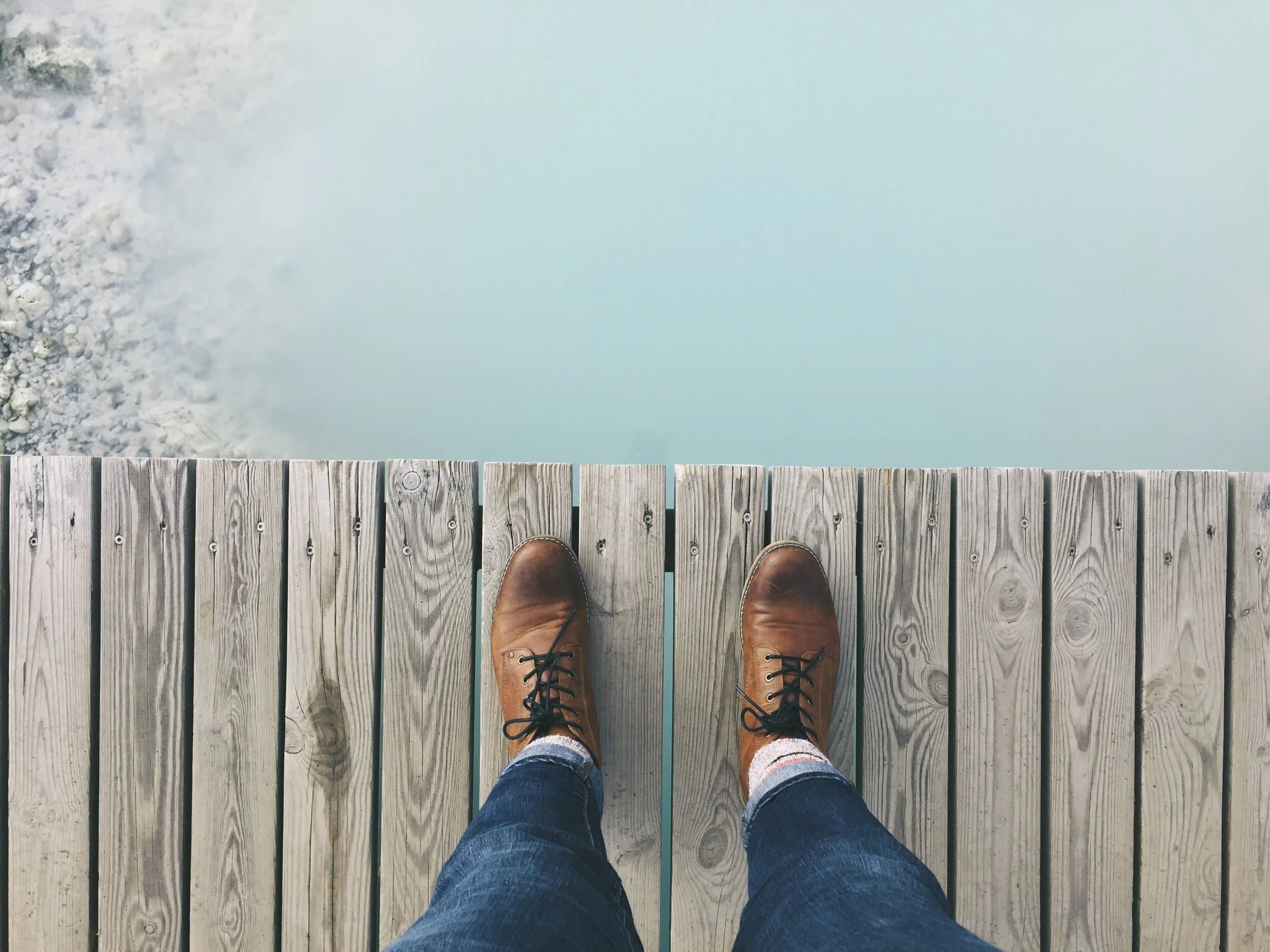 Looking down at a pair of boots on a wooden jetty above still water