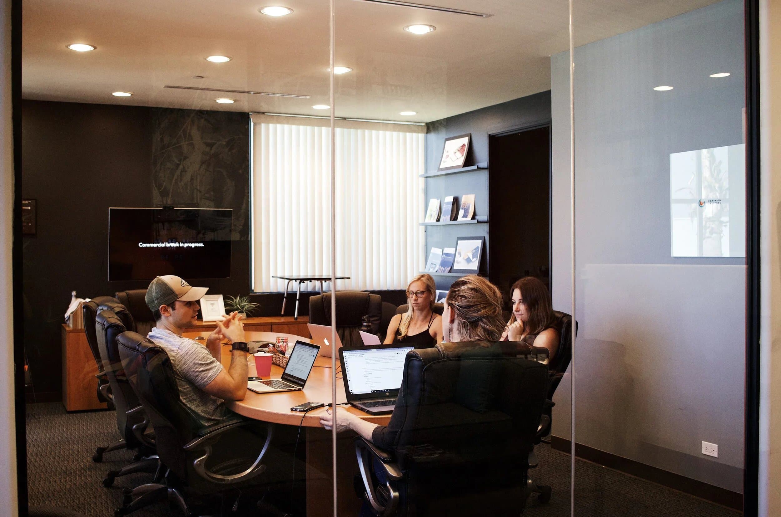 A small team working around a meeting table in a glass-walled office